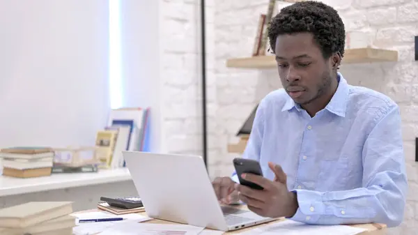 Smart African Guy met behulp van smartphone en laptop — Stockfoto