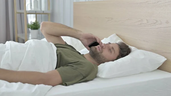 Young Man talking on his Smartphone in Bed — Stock Photo, Image