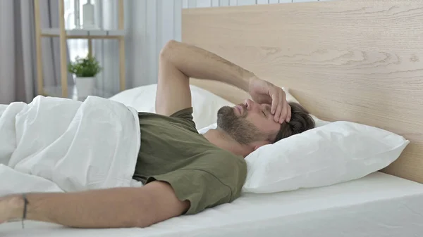 침대에 누워있는 동안 두통을 가진 젊은 남자를 강조 — 스톡 사진