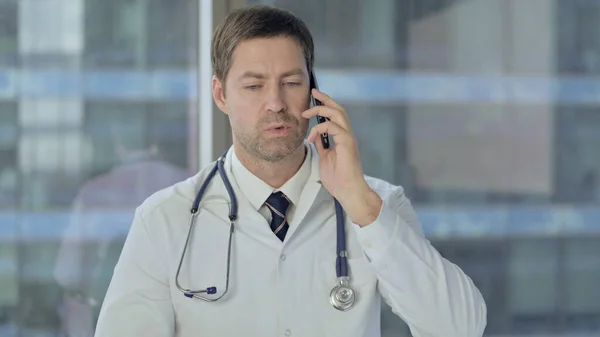 Доктор среднего возраста разговаривает по телефону с пациентом — стоковое фото