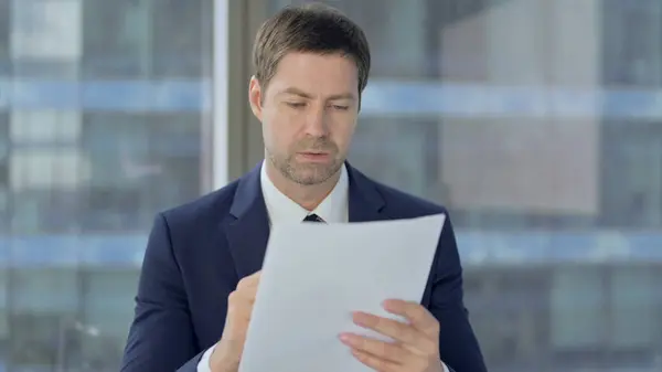 Geschäftsmann mittleren Alters studiert Dokumente bei der Arbeit — Stockfoto