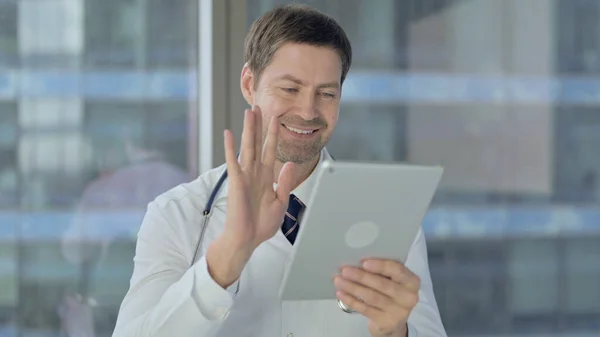 Médico de mediana edad hablando para el chat de vídeo en la tableta —  Fotos de Stock
