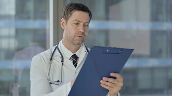 Серьезный врач среднего возраста, изучающий медицинские документы, бумажную работу — стоковое фото