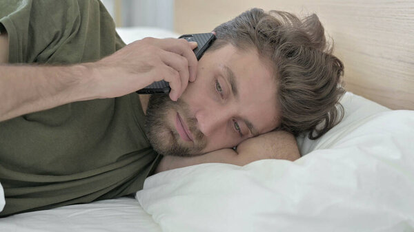 Close-up of Young Man talking on Smartphone in Bed