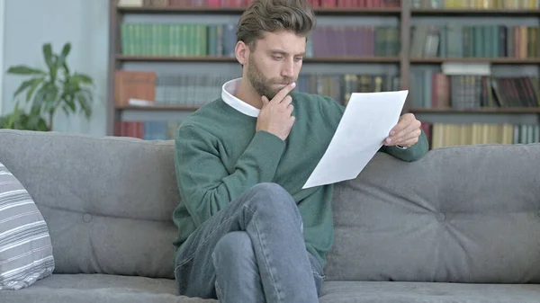 Задумчивый человек сидит на диване и изучает документы — стоковое фото