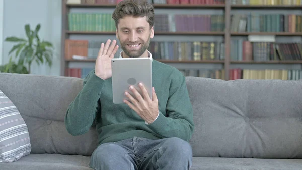 Happy Man Doing Video Chat on Tablet while Sitting on Sofa — стоковое фото