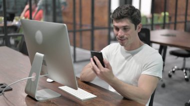 Genç adam iş yerinde akıllı telefon kullanıyor.