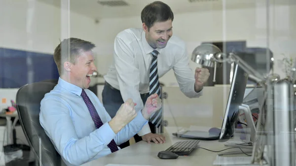 Зрелый бизнесмен использует офисный компьютер и празднует успех с коллегой — стоковое фото