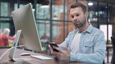 Genç adam iş yerinde akıllı telefon kullanıyor.