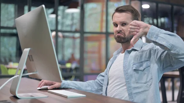 Junger Mann zeigt Daumen nach unten, während er am Computer arbeitet — Stockfoto