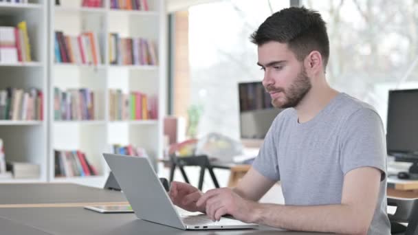 Mladý muž s notebookem s úsměvem na fotoaparátu v kanceláři — Stock video