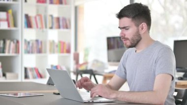 Ofiste dizüstü bilgisayar kullanarak öksüren genç adam.