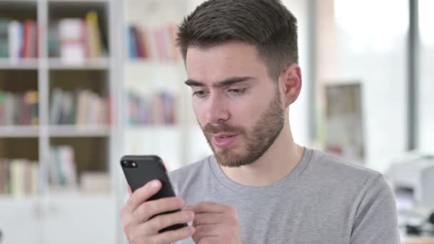 Retrato del joven reaccionando a la pérdida en el teléfono inteligente — Vídeos de Stock