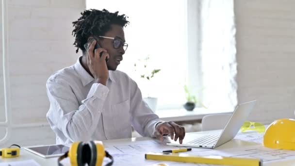 Ingegnere di architettura africano con computer portatile che parla su smartphone in ufficio — Video Stock