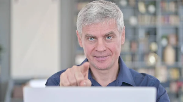 Porträt eines Mannes mittleren Alters, der mit dem Finger auf die Kamera zeigt und am Laptop arbeitet — Stockfoto