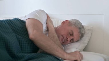 Orta yaşlı adam tek başına yatakta uyumaya çalışıyor.