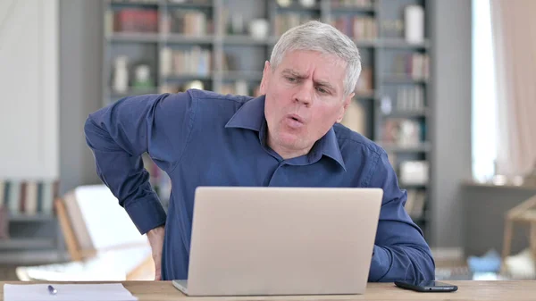 Müder Mann mittleren Alters mit Rückenschmerzen bei der Arbeit am Laptop — Stockfoto