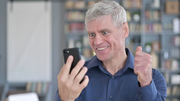 Porträt eines Mannes mittleren Alters, der auf dem Smartphone mit der Faust feiert — Stockfoto