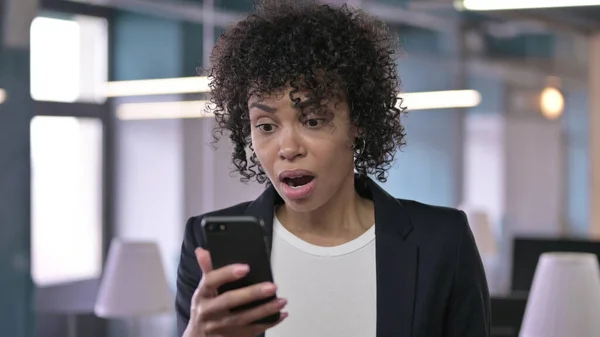 Portrait of Shocked African Businesswoman reacting to Loss on Smartphone