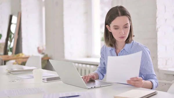 Fokuserad ung kvinna Läsa dokument och arbeta på laptop — Stockfoto