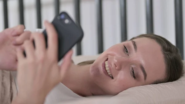 Młoda kobieta za pomocą rozmytego smartfona w łóżku — Zdjęcie stockowe