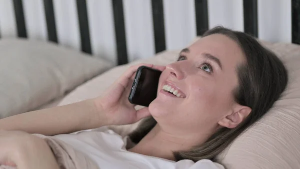 Jovem mulher falando no smartphone na cama — Fotografia de Stock
