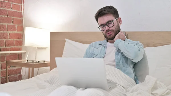 Fleißiger junger Mann mit Brille hat Nackenschmerzen im Bett — Stockfoto