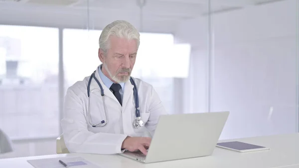 Medico anziano concentrato che lavora sul computer portatile — Foto Stock