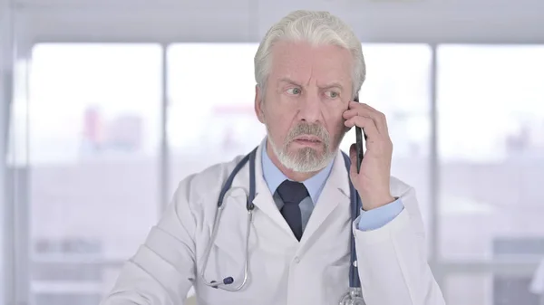 Porträt eines alten Arztes im Gespräch mit dem Smartphone in der Klinik — Stockfoto