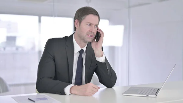 Empresario serio de mediana edad que habla en el teléfono inteligente en la oficina — Foto de Stock