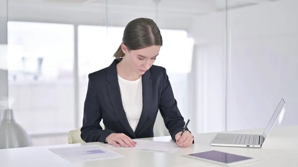 Jeune femme d'affaires concentrée écrivant sur le papier dans un bureau moderne — Photo