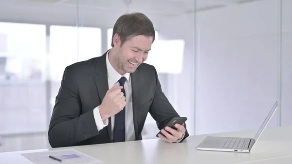 Empresario de mediana edad celebrando el éxito en el teléfono inteligente — Foto de Stock