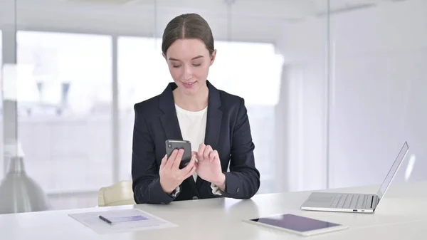 Jeune femme d'affaires ciblée utilisant un téléphone intelligent au bureau — Photo