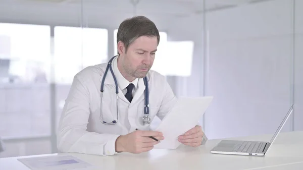 Εργατικός Μεσήλικας Γιατρός Διαβάζοντας Έγγραφα στην Κλινική — Φωτογραφία Αρχείου
