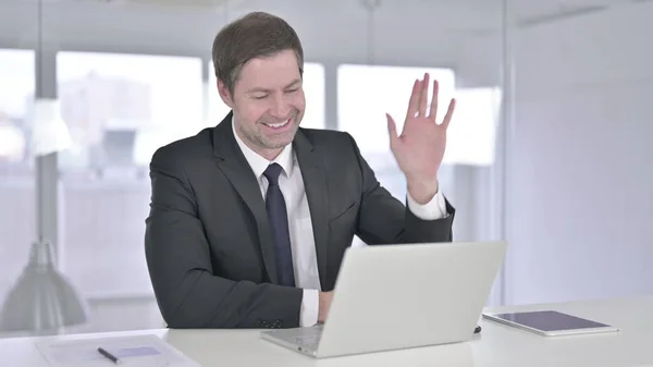 Веселый бизнесмен среднего возраста, который ведет видео-чат на ноутбуке — стоковое фото