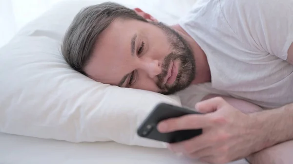 Primer plano de Barba Joven utilizando Smartphone en la cama —  Fotos de Stock