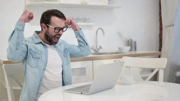 Überraschter junger Mann mit Bart feiert Erfolg auf Laptop — Stockfoto