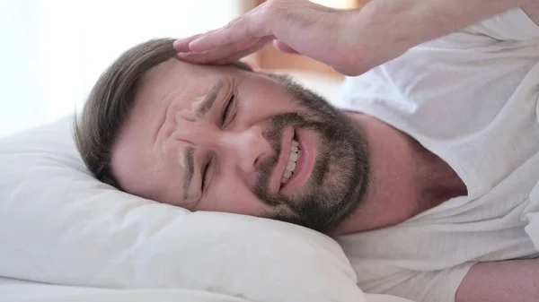 Close up de sem sono barba jovem homem com dor de cabeça na cama — Fotografia de Stock
