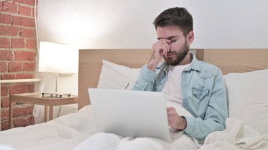 Baş ağrısı olan genç adam laptopta çalışıyor.