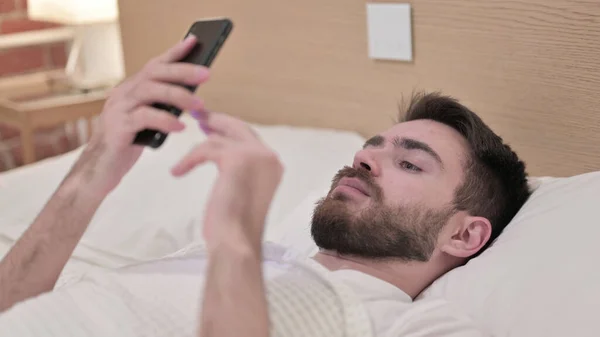 Jovem bonito usando Smartphone na cama — Fotografia de Stock