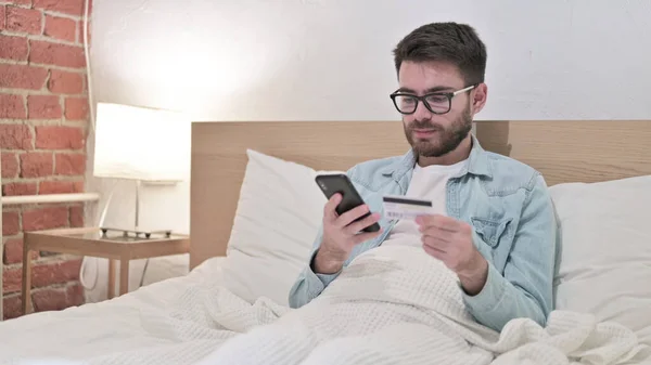 Привлекательный молодой человек в очках Успех в онлайн-оплаты в постели — стоковое фото