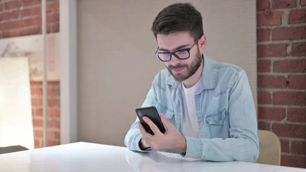 Attractive Young Man in Glasses Using Smartphone in Office — Stock Photo, Image