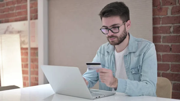Hombre joven enfocado en gafas que hace el pago en línea en el ordenador portátil — Foto de Stock
