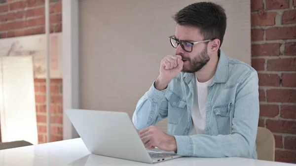 Kranker junger Mann mit Brille arbeitet am Laptop und hustet — Stockfoto
