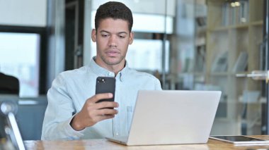 Akıllı telefon ve dizüstü bilgisayar kullanan genç bir Afrikalı.