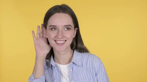 Jonge vrouw luisteren geheim, geïsoleerd op gele achtergrond — Stockfoto