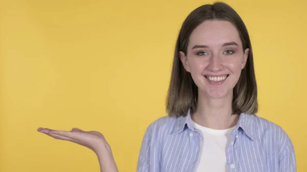 Młoda kobieta prezentuje produkt na stronie, żółte tło — Zdjęcie stockowe