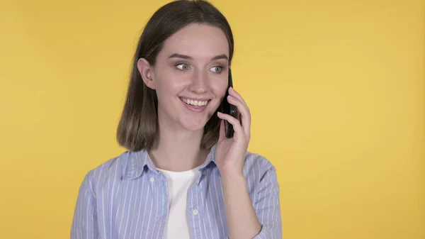 Молодая женщина говорит на смартфоне на жёлтом фоне — стоковое фото