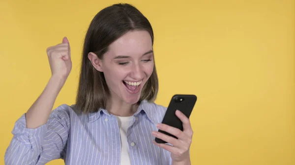 Jovem mulher animada comemorando o sucesso no smartphone, fundo amarelo — Fotografia de Stock