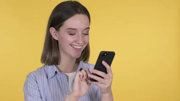 Młoda kobieta przeglądająca smartfon na żółtym tle — Zdjęcie stockowe